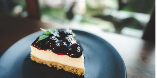 Käsekuchen mit Kirschen und Minzblättchen auf grauem Teller.