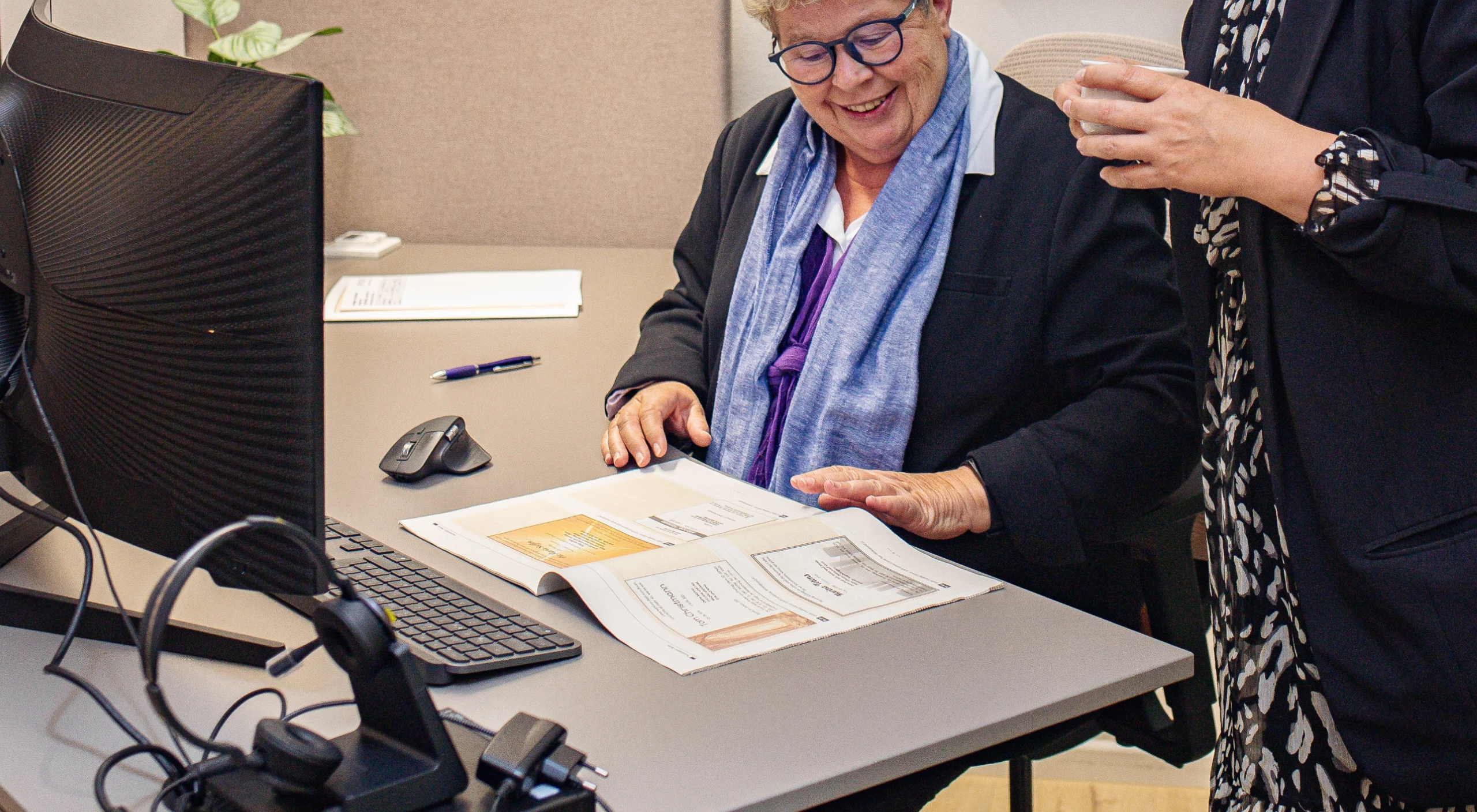 Mitarbeiter zeigt Leuchttunrm-Urne älterem Herrn. Rechts im Regal und hinten in einem Ruderboot weitere dekorierte Urnen
