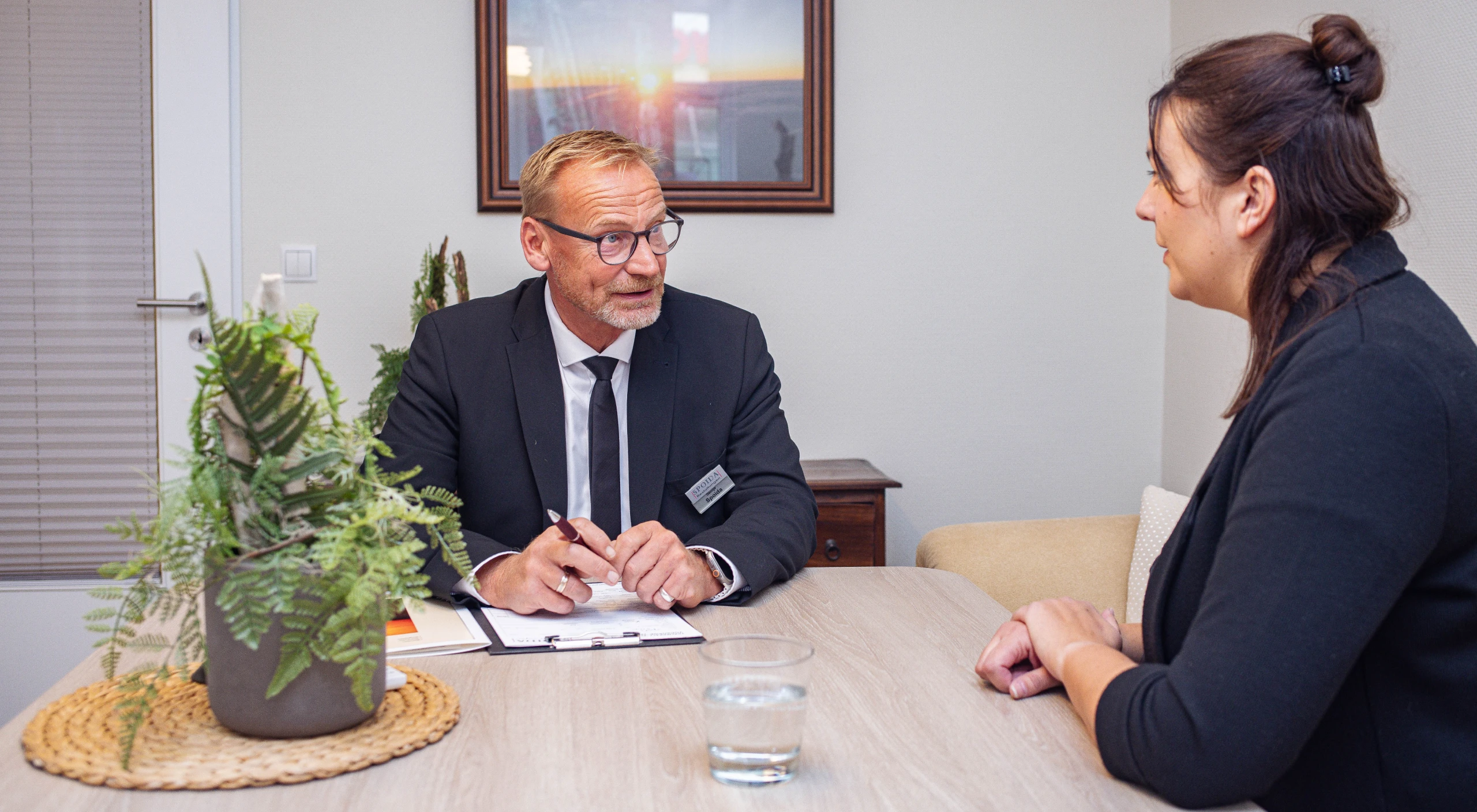George Spoida mit Unterlagen am Tisch im Beratungsgespräch mit einer jüngeren Frau.